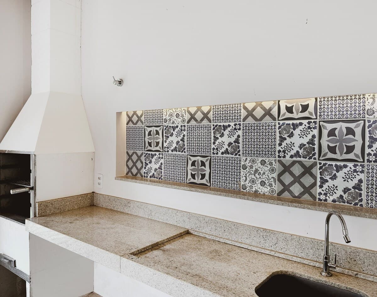 Churrasqueira coberta da Casa Mato Verde, com bancada de granito e faixa de azulejo português preto e branco