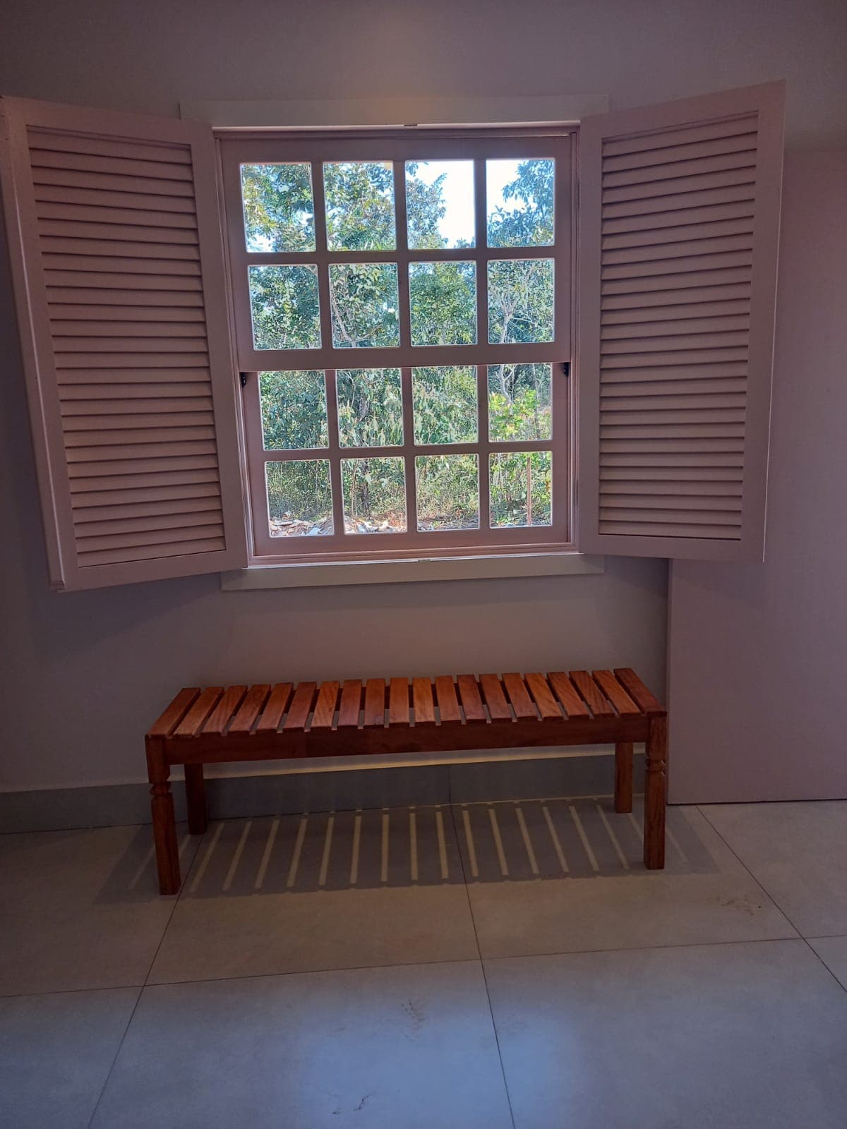 Janela colonial com veneziana e banco de madeira na Casa Ipê Rosa